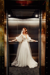 bride in a white elegant dress, with a long veil stands in a dark lift.