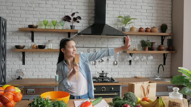 An attractive young woman sings and dances while preparing dinner for her loving boyfriend.A happy young housewife in a good mood sings funny into a wooden spoon and dances merrily in her kitchen