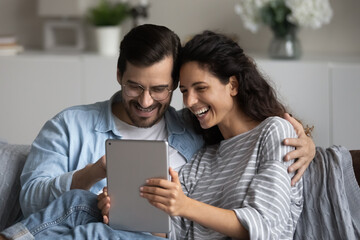 Smiling young multiracial couple look at tablet screen talk speak on webcam video call on gadget online. Happy multiethnic man and woman use pad device browse wireless internet. Technology concept.