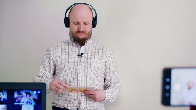 English language training. A bald man with a beard is doing distance learning online using flashcards to learn the alphabet. Man in headphones and microphone