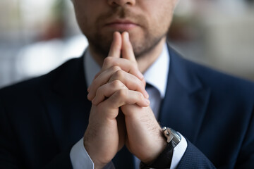 Clasped hands of business leader touching chin in deep thoughts, making decision. Thoughtful businessman thinking of project plan, pondering on deal, contract, partnership offer. Cropped close up