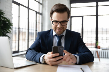 Happy businessman using online app on smartphone at office workplace. Employee wearing suit and...