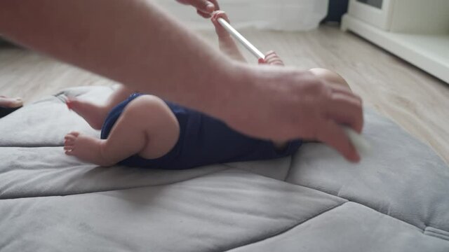 Father doing exercise with his baby boy on activity gym play mat on floor in living room, father puts bar in baby hands improving grip. High quality 4k footage