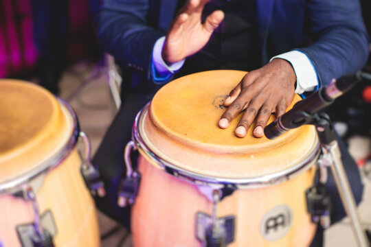 Bongo drummer percussionist performing on a stage with conga drums set kit during jazz rock show performance, with latin cuban band performing in the background, drummer point of view