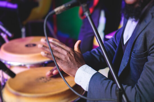 Bongo drummer percussionist performing on a stage with conga drums set kit during jazz rock show performance, with latin cuban band performing in the background, drummer point of view