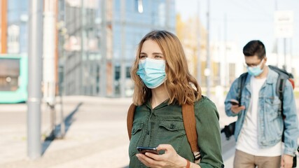 Portrait of Caucasian travelers in masks on street passing health control showing vaccination digital passport on smartphone man scan QR code vaccine certificate on cellphone and measuring temperature