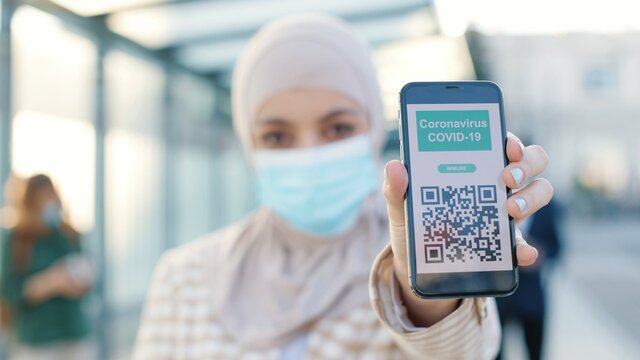 Muslim women in medical mask showing an International Vaccination Certificate COVID-19 QR code on smartphone. Close up concept. Vaccinated person using digital health passport app in mobile phone