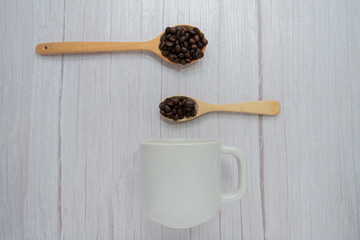 Roasted coffee beans in wooden spoon on wooden floor background.
