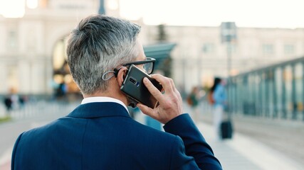 Rear of unrecognizable male in suit walking on street calling on cellphone. Man walk outdoors and...