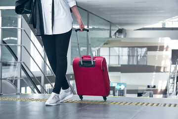woman traveler with luggage in the airport or train station; legs and suitcase close-up