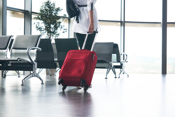 woman traveler with luggage in airport or train station waiting room; legs and suitcase close-up