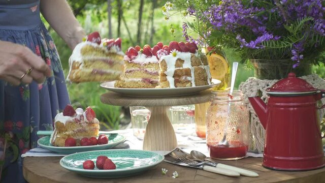girl putting pieces of homemade strawberry biscuit on a plates. Breakfast on a dinner table in the private summer garden
