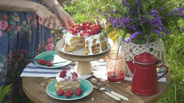 girl putting pieces of homemade strawberry biscuit on a plates. Breakfast on a dinner table in the private summer garden
