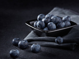 Ripe blueberries in black bowl on dark grey background. Selective focus on blueberies lying on table