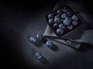 Ripe blueberries in black bowl on dark grey background. Top view