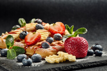 Tasty waffles with berries, mint and sweet sauce on slate serving board on grey background. Sweet meal. Dessert