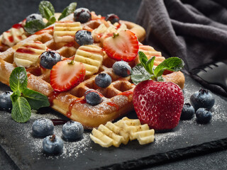 Tasty waffles with berries, mint and sweet sauce on slate serving board on grey background. Sweet meal. Dessert