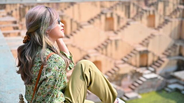 Cheerful woman wearing colorful cloth enjoy the view sitting over Indian old step-well in Rajasthan. slow-motion footage
