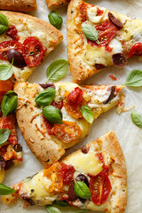 Vegetarian pizza with colorful cherry tomatoes, olives and fresh basil leaves, cut into portions on a white background top view