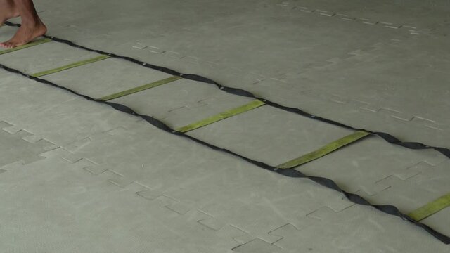 Man and woman training in the gym. He teaches and she repeats on the agility ladder mounted on the mat. Only the feet of both appear. Physical preparation training.