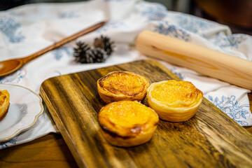 Egg tarts, homemade traditional Portuguese dessert, pastel de nata, wood cutting board, vintage fabric and utensils on a white dish on a wooden table. Copy space.