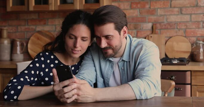Overjoyed young loving family couple looking at smartphone screen, getting message with good news, celebrating online lottery gambling giveaway win, receiving low price discount shopping promo code.