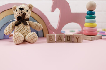 Wooden pyramid, toys, a horse, word baby on pastel pink background. Trendy cute baby first toys. Eco-friendly, set of accessories for kids. Toys for kindergarten, preschool or daycare. Close up