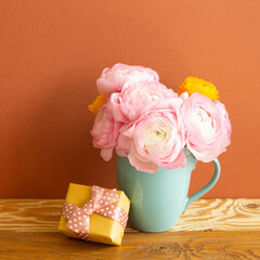 Yellow gift box and pink ranunculus flowers bouquet on wooden table. brown background