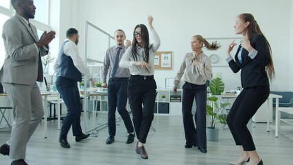Pretty Asian woman is dancing with coworkers in formal clothing during teambuilding party in office. Modern youth lifestyle and corporate culture concept.