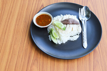 Chicken rice, top view with spoon and fork in the black dish isolated on wooden background closeup.
