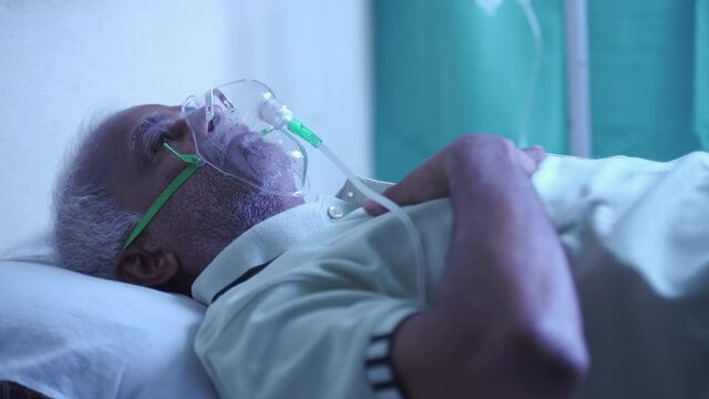 Old man feeling uncomfortable rubbing his chest while breathing on ventilator oxygen mask - ill patient suffering breathlessness due to coronavirus covid-19 dyspnea at hospital.