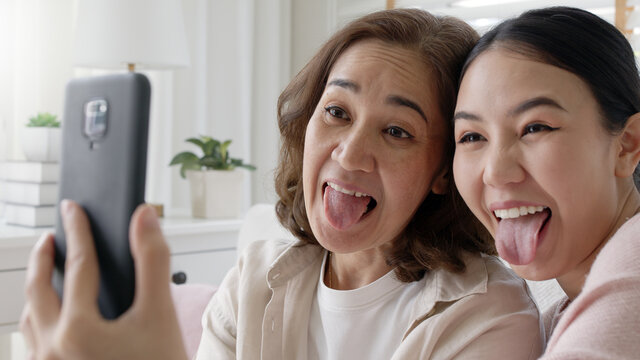 Attractive beautiful two people asia young lady girl use mobile phone take photo picture video camera overjoy sit at home sofa couch have good time day together quarantine in mum healthy health care.