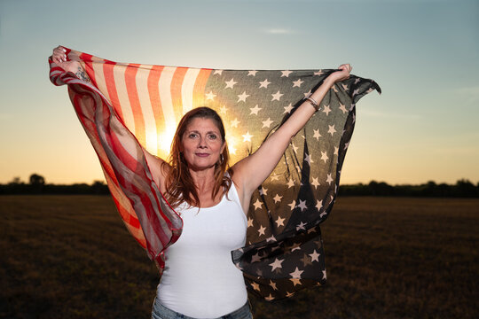 Proud middle aged patriotic American woman in field with flag at sunset