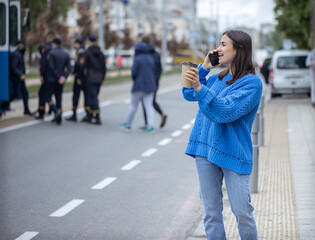 Fototapeta premium Stylish young girl speaks on the phone and holds coffee to go in her hand.