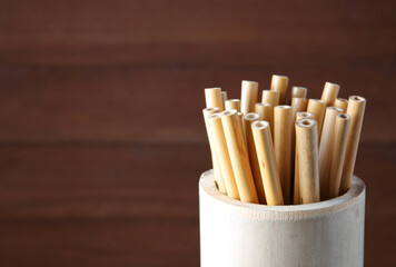 bamboo straw in bamboo cylinder on wood background with copy space ( straw from natural material / green product concept )
