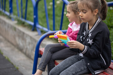 A little cheerful girl plays with a popular colorful toy antistress pop it.