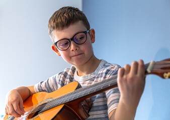 Little boy boy with glasses plays the classical guitar close up.