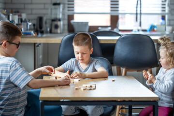 Cute children play a board game with wooden cubes on the table at home.