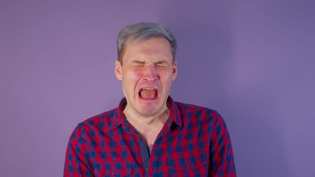Close up of young man getting slapped in face on purple background. Unrecognizable woman hits cheeky guy on cheek deservedly.