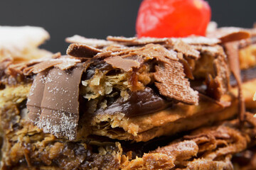 Puff pastry cakes with powdered sugar and cream and another with chocolate and a cherry on top on the wooden table. Macro close up. Selective focus.