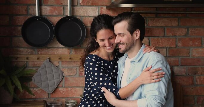 Happy loving young married family couple cuddling indoors, looking in distance dreaming or visualizing common future, feeling excited of new beginning in own dwelling, showing romantic relations.
