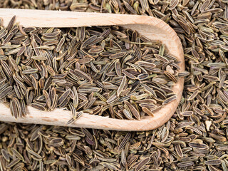 wooden scoop on pile of kala zeera seeds closeup