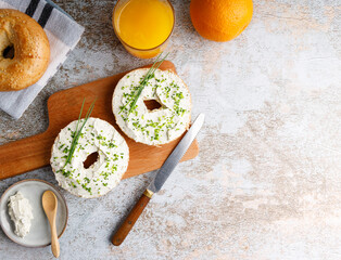 Breakfast table with bagels fresh cheese. Bagels with fresh cheese and herbs on a breakfast table , with fresh orange juice and coffee on the side.