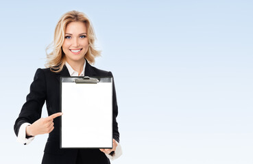 Portrait of young businesswoman showing blank clipboard, with copyspace area for text or slogan, on blue background. Success in business, job and education concept.
