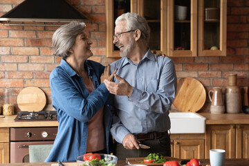 Happy mature grey haired couple of vegans cooking vegetarian salad natural organic food standing...