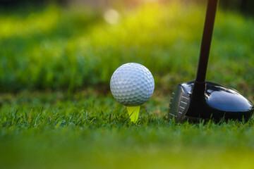 Golf club and golf ball on tee close up in grass field with morning sunshine.