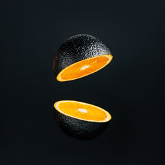 Orange painted on black and cut in half levitating against black background. Creative food concept. Unique and unusual fruit composition.