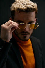 Fototapeta premium man blond in glasses and an orange sweater jacket dark background model close-up