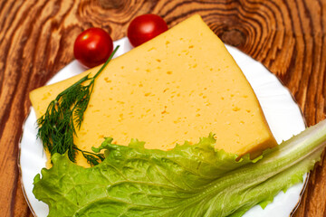 a piece of cheese lettuce cherry tomatoes and herbs on a white plate on a wooden table