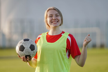 Happy female football player in sportwear celebrating victory, holding soccer ball